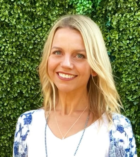Woman with blonde hair smiling in front of a green hedge