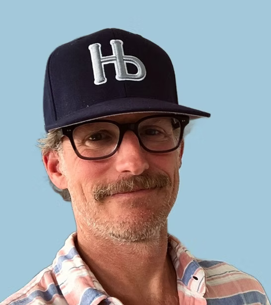 Man wearing a black cap with 'HB' logo and glasses against a light blue background