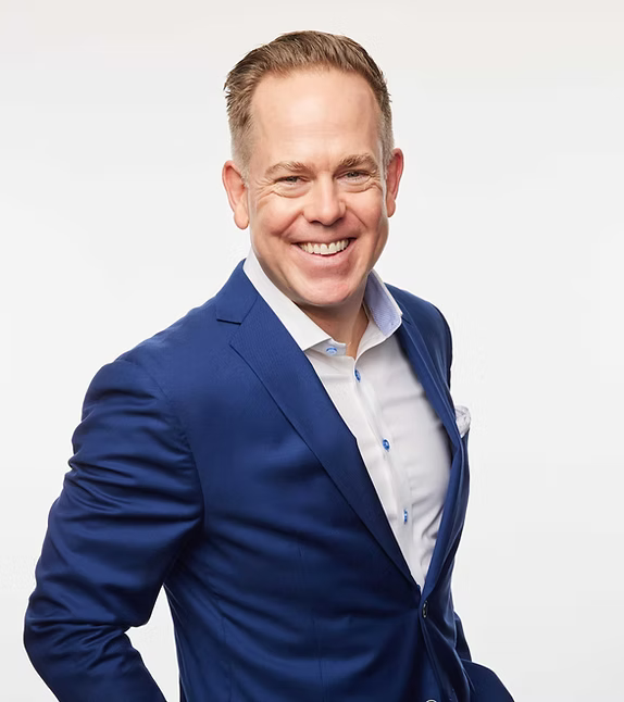 Man wearing a blue suit jacket over a white shirt on a light gray background